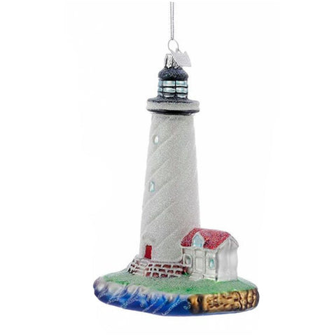 White lighthouse by the sea ornament with tall white tower, red-roofed cottage, ocean wave base, and silver hanging cord.