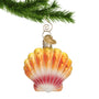Glass Seashell Ornament Scalloped Shell in ombre from Pinks to orange hanging from a gold swirl hook on a Christmas tree branch