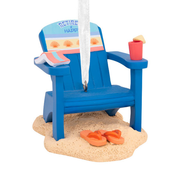 Retirement Ornament Blue Adirondack chair with saying Retired and Happy on the beach featuring a book and drink on the arms of chair and sandals in a patch of sand